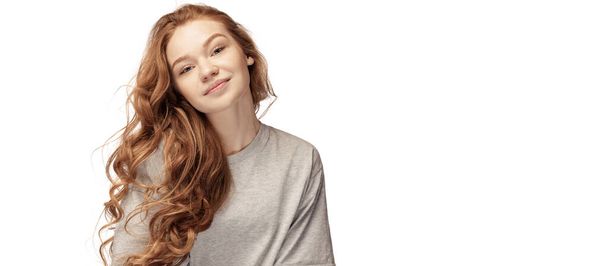 Happy redhead young girl with long curly hair looking at camera with light smile isolated on white background. Student in casual clothes. Concept of youth, beauty, life. Copy space for ad. Flyer - Foto, Imagem