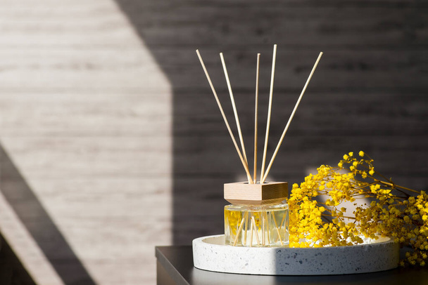 Transparent bottle of aroma diffuser on the terazzo podium on blurred room background. Eau de parfum for home presentation on a podium with field flowers. Trending concept in natural materials. - Photo, Image
