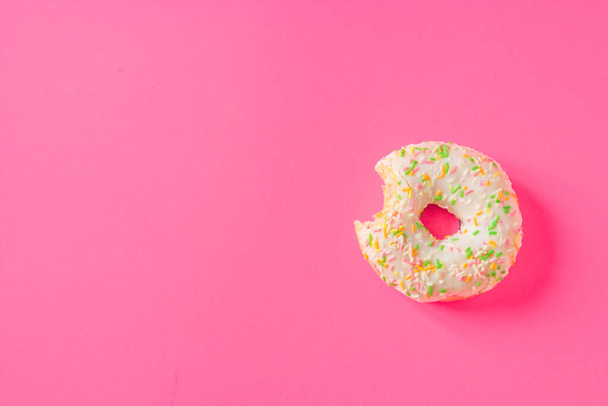 Donut único revestido com uma geada branca e polvilhas coloridas, isolado em um fundo rosa. Deitado. Vista superior. Dia Nacional do Donut. - Foto, Imagem