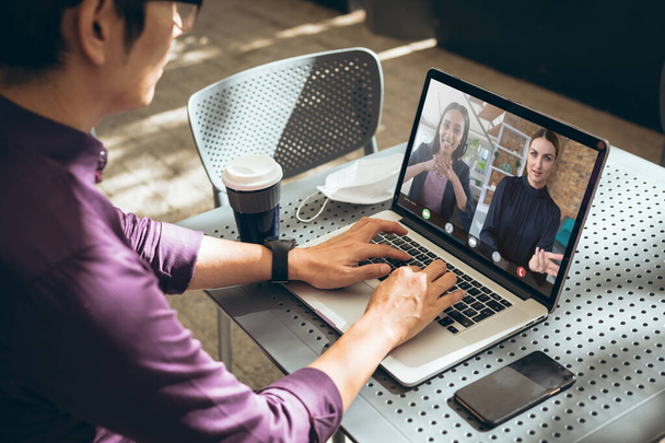 Businessman discussing work with multiracial female coworkers through video call on laptop. unaltered, online, wireless technology, video conference, internet, business, teamwork, office, covid. - Photo, image