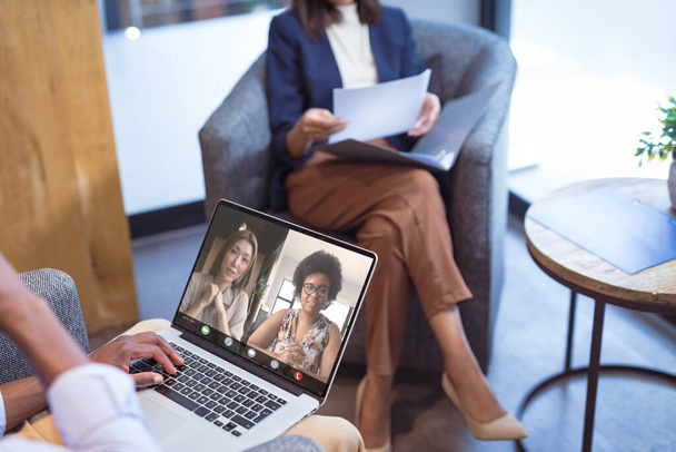 Multiracial businesswomen video calling while working in office. unaltered, online, technology, video conference, discussion, internet, business, teamwork, wireless technology. - Фото, изображение