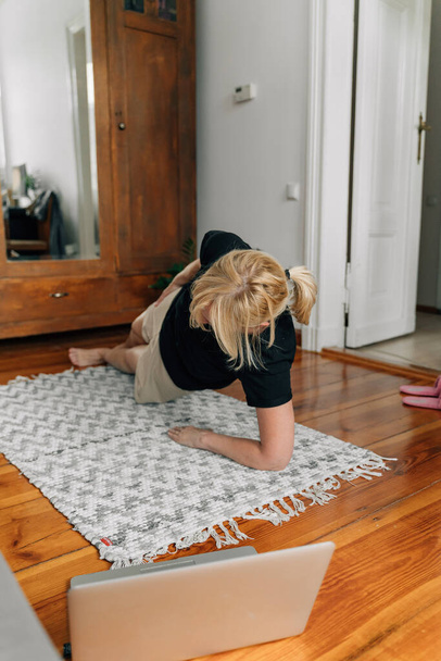 mature woman at home doing sport yoga on the floor with laptop online classes . High quality photo - Φωτογραφία, εικόνα
