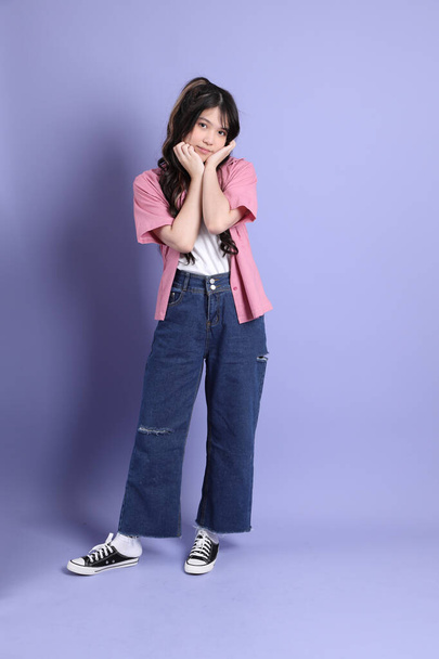 La linda chica asiática joven con ropa casual de pie sobre el fondo púrpura. - Foto, Imagen
