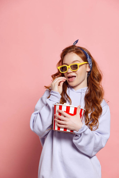 Watch melodrama. Young beautiful woman in casual outfil eating popcorn and watching movie isolated on pink background. Concept of emotions, facial expression, sales, ad, fashion and beauty - Foto, afbeelding