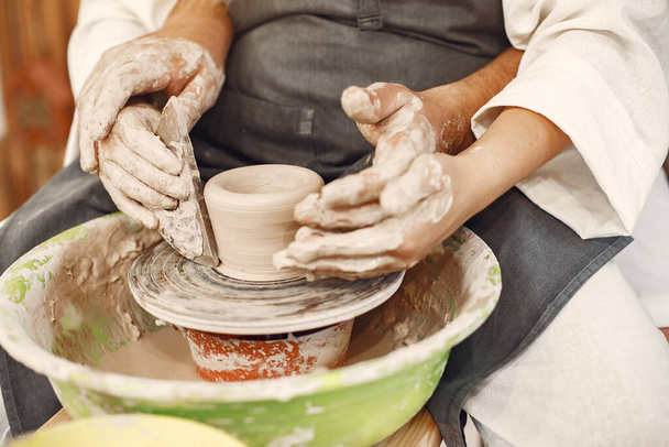 Mutual creative work. Young beautiful couple in casual clothes and aprons. People creating a bowl on a pottery wheel in a clay studio. - Foto, Imagem