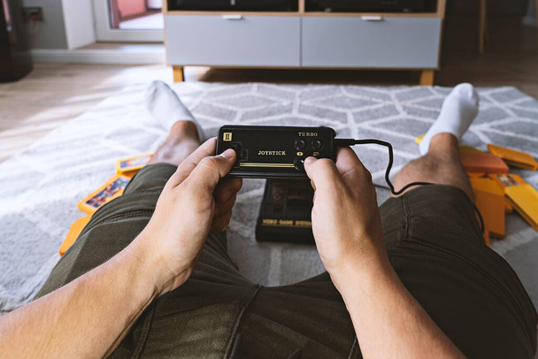 Male hands holding joystick from video-game console against background of home interior and TV-screen. First-person view. Home entertainment concept - Photo, Image