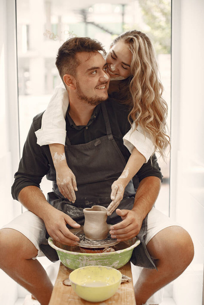 Mutual creative work. Young beautiful couple in casual clothes and aprons. People creating a bowl on a pottery wheel in a clay studio. - Foto, Imagen