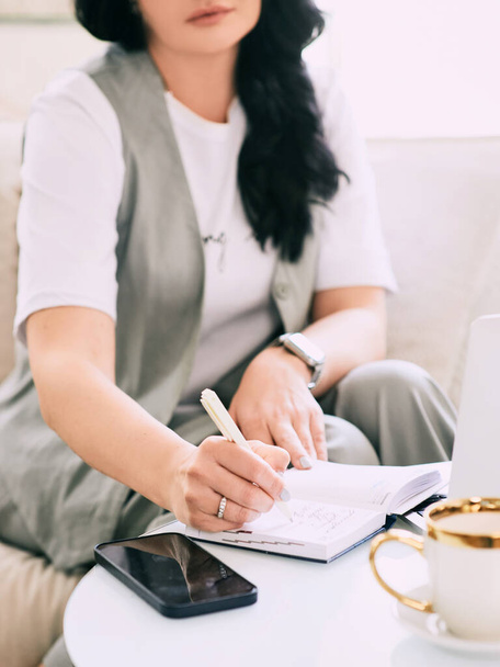 γυναίκα κάθεται στον καναπέ και κρατά σημειώσεις στο σημειωματάριό της. Επιχειρήσεις, αναλυτική, εκπαίδευση - Φωτογραφία, εικόνα