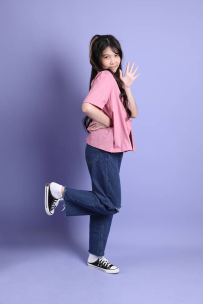 Το χαριτωμένο νεαρό κορίτσι της Ασίας με casual ρούχα στέκεται στο μωβ φόντο. - Φωτογραφία, εικόνα