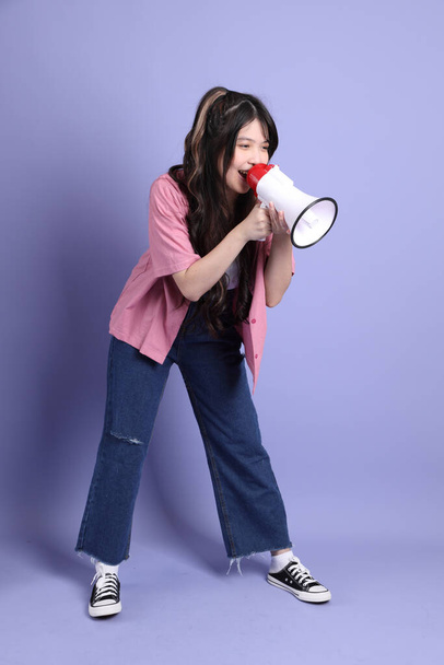 The cute young Asian girl with casual clothes standing on the purple background. - Zdjęcie, obraz