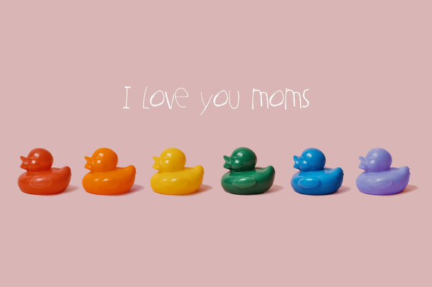 de tekst Ik hou van jullie moeders en een aantal rubberen eenden van verschillende kleuren vormen de regenboog vlag op een roze achtergrond - Foto, afbeelding