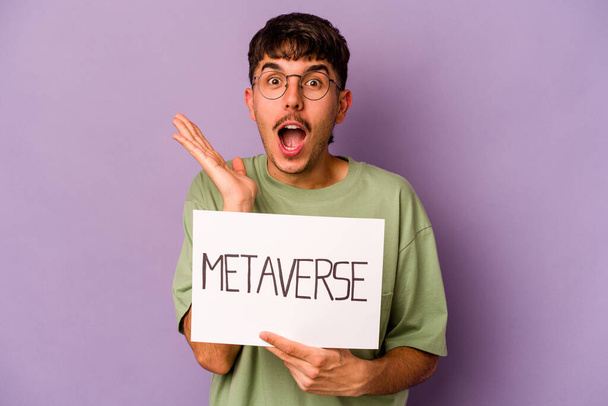 Young hispanic man holding meta verse placard isolated on purple background surprised and shocked. - Photo, Image