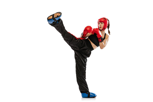 High kick. One female boxer in boxing gloves and helmet training isolated on white studio background. Sport, competition, hobby, results, success concept. Sportive woman practicing in boxing. - Φωτογραφία, εικόνα