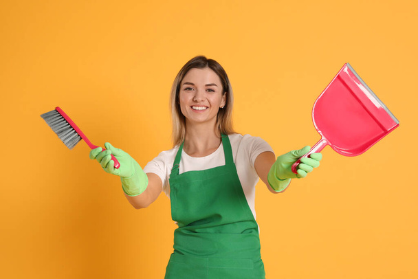 Young woman with broom and dustpan on orange background - Φωτογραφία, εικόνα