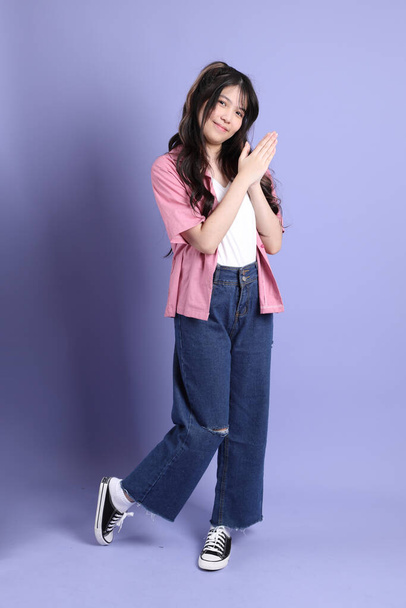 La linda chica asiática joven con ropa casual de pie sobre el fondo púrpura. - Foto, imagen