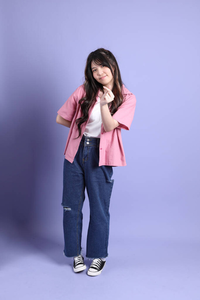 De schattige jonge Aziatische meisje met casual kleding staan op de paarse achtergrond. - Foto, afbeelding