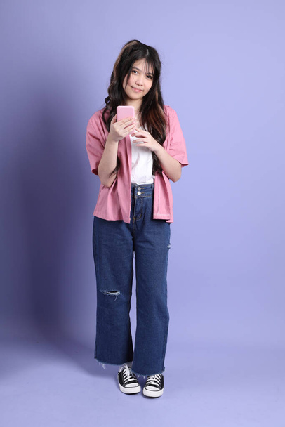 The cute young Asian girl with casual clothes standing on the purple background. - 写真・画像