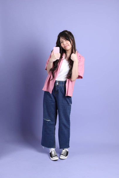 La linda chica asiática joven con ropa casual de pie sobre el fondo púrpura. - Foto, imagen