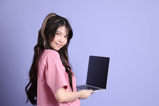 La jolie jeune fille asiatique avec des vêtements décontractés debout sur le fond violet. - Photo, image