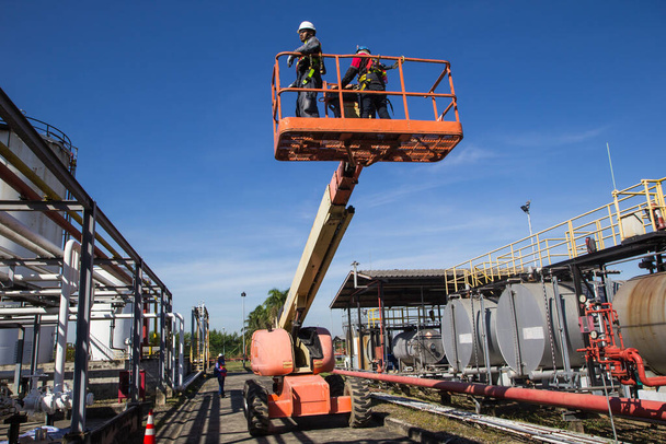 Twee mannelijke industrie werken op hoog in een boom lift inspectie van pijpleiding olie - Foto, afbeelding