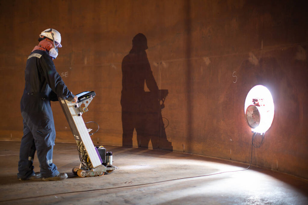 El tanque de escaneo del piso de inspección del trabajador masculino de la pared oxidada pierde la placa inferior del grueso adentro a confinado - Foto, imagen