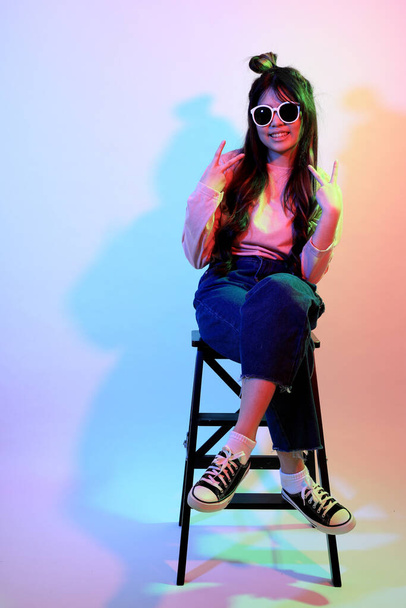 La linda chica asiática joven con ropa casual posando bajo el color del gel relámpago en el estudio. - Foto, Imagen