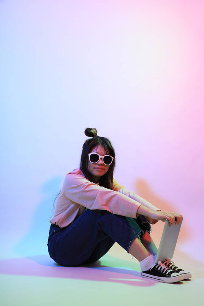 Мила азіатська дівчина з випадковим одягом, що стоїть під кольоровою блискавкою в студії.. - Фото, зображення