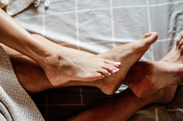 Two pairs of human legs in bed close up, man and woman lying in bed, intimate intimacy of the couple. - Foto, Imagem