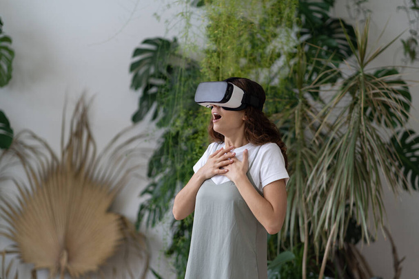 Menina emocionalmente chocada no fone de ouvido VR imerso no mundo virtual 3D cheio de emoções e impressões, gritando durante a primeira experiência de realidade virtual. Mulher usando tecnologia interativa em casa jardim - Foto, Imagem