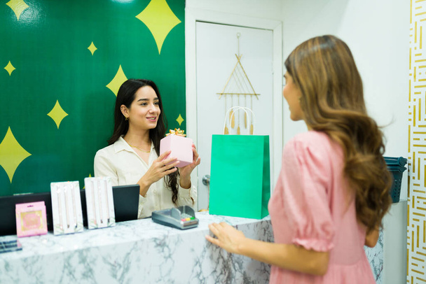 ラテン語の営業担当者は、化粧品店での買い物のために女性の顧客にギフトボックスを与えます  - 写真・画像