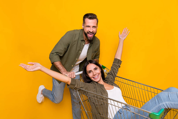 Profile side photo of young lovely couple have fun ride cart store isolated over yellow color background. - Fotoğraf, Görsel