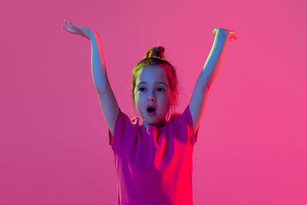 Wow kid emotion. Portrait of cute little girl, kid wearing pink t-shirt posing isolated on magenta color background. Concept of children emotions, fashion, beauty, school and ad concept. - Foto, Bild