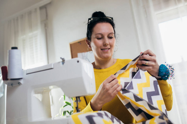 彼女の家でミシンをかけている女性。縫製機械における女性のシームレスストレス作業 - 写真・画像