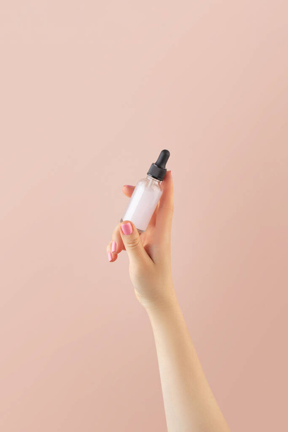 A mock-up of a glass dropper with skin oil in a womans hand on a light pink background. - Foto, immagini