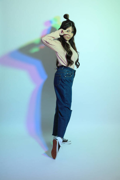 La jeune fille asiatique mignonne avec des vêtements décontractés posant sous la foudre de couleur de gel en studio. - Photo, image