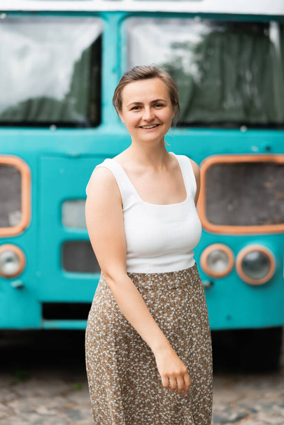 Een glimlachend mooi blondje staat op de achtergrond van de oude schoolbus. Levensstijl concept - Foto, afbeelding