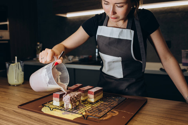 Женщина наливает сливки на тарелку из слоистого коричневого торта с малиной сверху - Фото, изображение