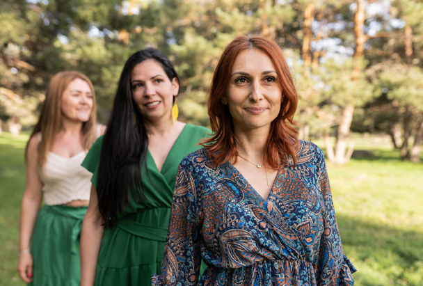 Ormandaki yetişkin beyaz kadınlar elbise giyip kızıl saçlı kadınlara odaklanıyor. - Fotoğraf, Görsel