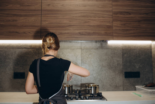 Young woman frying eggs for breakfast at kitchen stove, view from the back - Foto, afbeelding