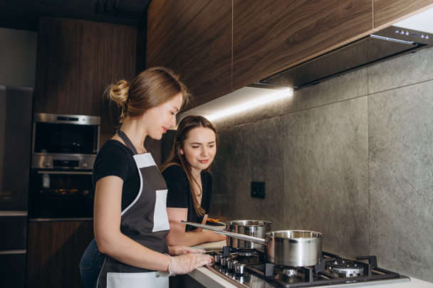 Two beautiful friends in aprons prepare sweets at the stove in a modern kitchen. Girls confectioners - Valokuva, kuva