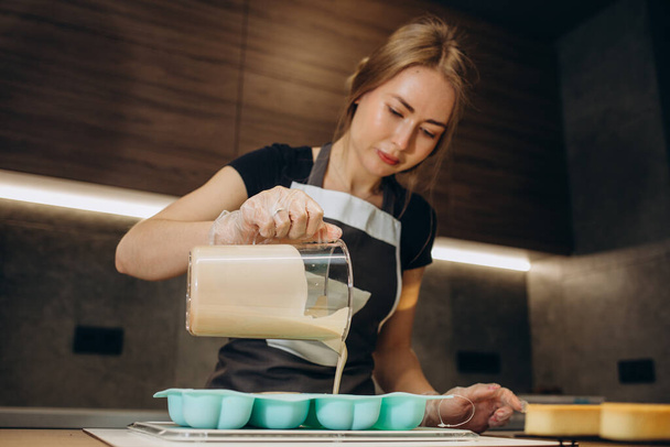 Jonge vrouwelijke banketbakker giet vloeibare mousse in een mal. Bereiding van cake, dessert in een professionele keuken. - Foto, afbeelding