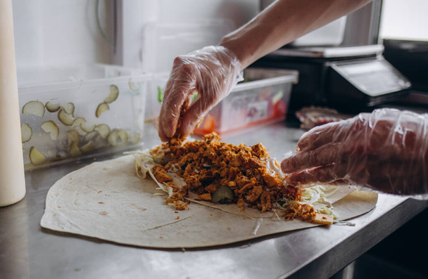 Mãos masculinas envolvendo envoltório shawarma tradicional com frango e legumes
 - Foto, Imagem