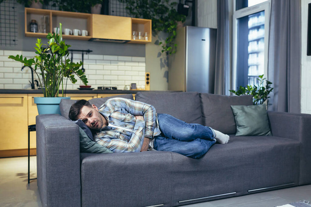 A young man is sleeping and lying on the couch at home. Tired, feeling bad, sick - Foto, Imagen