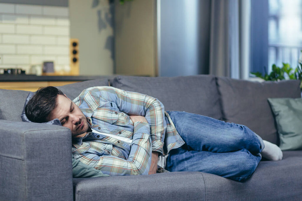 A young man is sleeping and lying on the couch at home. Tired, feeling bad, sick - Fotoğraf, Görsel