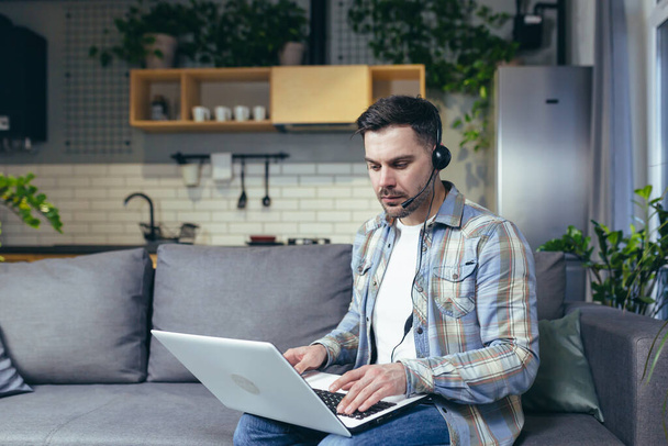 Young man working from home with laptop and in headphones. Talks on video call. Sitting on the couch. - Foto, imagen