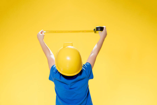A little boy in a protective construction helmet measures with a tape measure. - Foto, Imagem