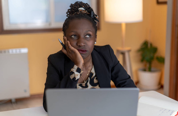 Genç siyahi bir kadının portresi çevrimiçi bir toplantıda bir dizüstü bilgisayar ile çalışan siyah ceketli bir hayvanla sıkılmış. - Fotoğraf, Görsel