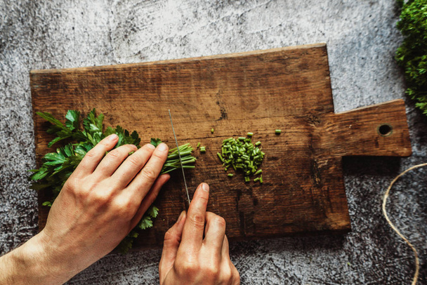 ένας άνθρωπος κόβει μαϊντανό με τα χέρια του σε καφέ ξύλινο πίνακα για σαλάτες ή άλλα πιάτα - Φωτογραφία, εικόνα