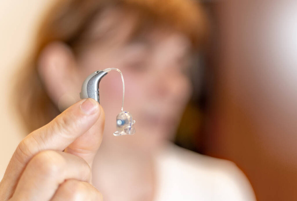 unrecognizable Lady showing a modern hearing aid held with two fingers - Foto, Bild