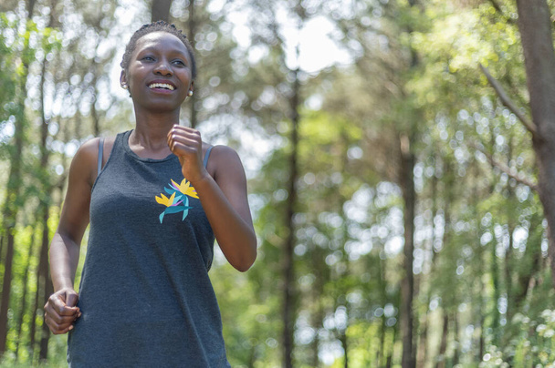  Genç bir spor kadını güneşli bir günde ormanda koşuyor. - Fotoğraf, Görsel